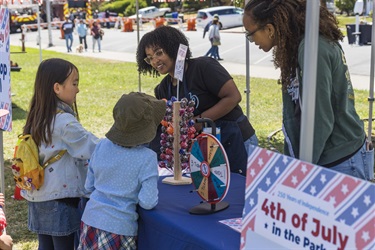 Two kids selecting prize from two Recreation staff members after playing Spin-it-to-win-it game at 4th of July in the Park