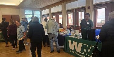 A group of people are gathered near resource tables at Homeowners & Tenants Resource Fair