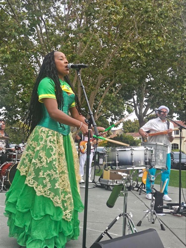 Musician on stage singing into microphone while playing a drum with sticks
